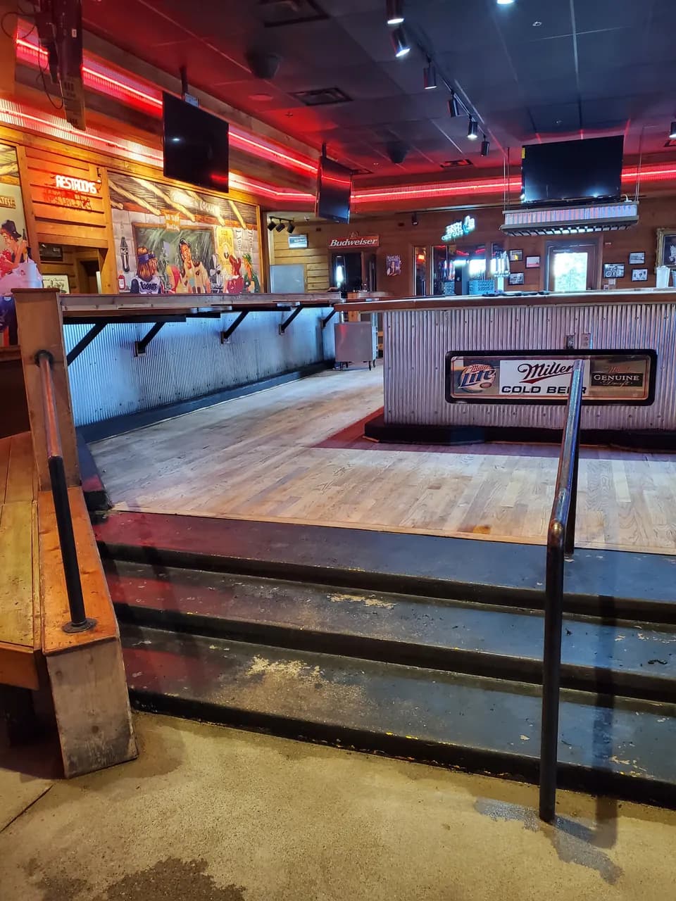 Bar interior with wood-paneled walls, overhead televisions and steps leading to a raised seating area