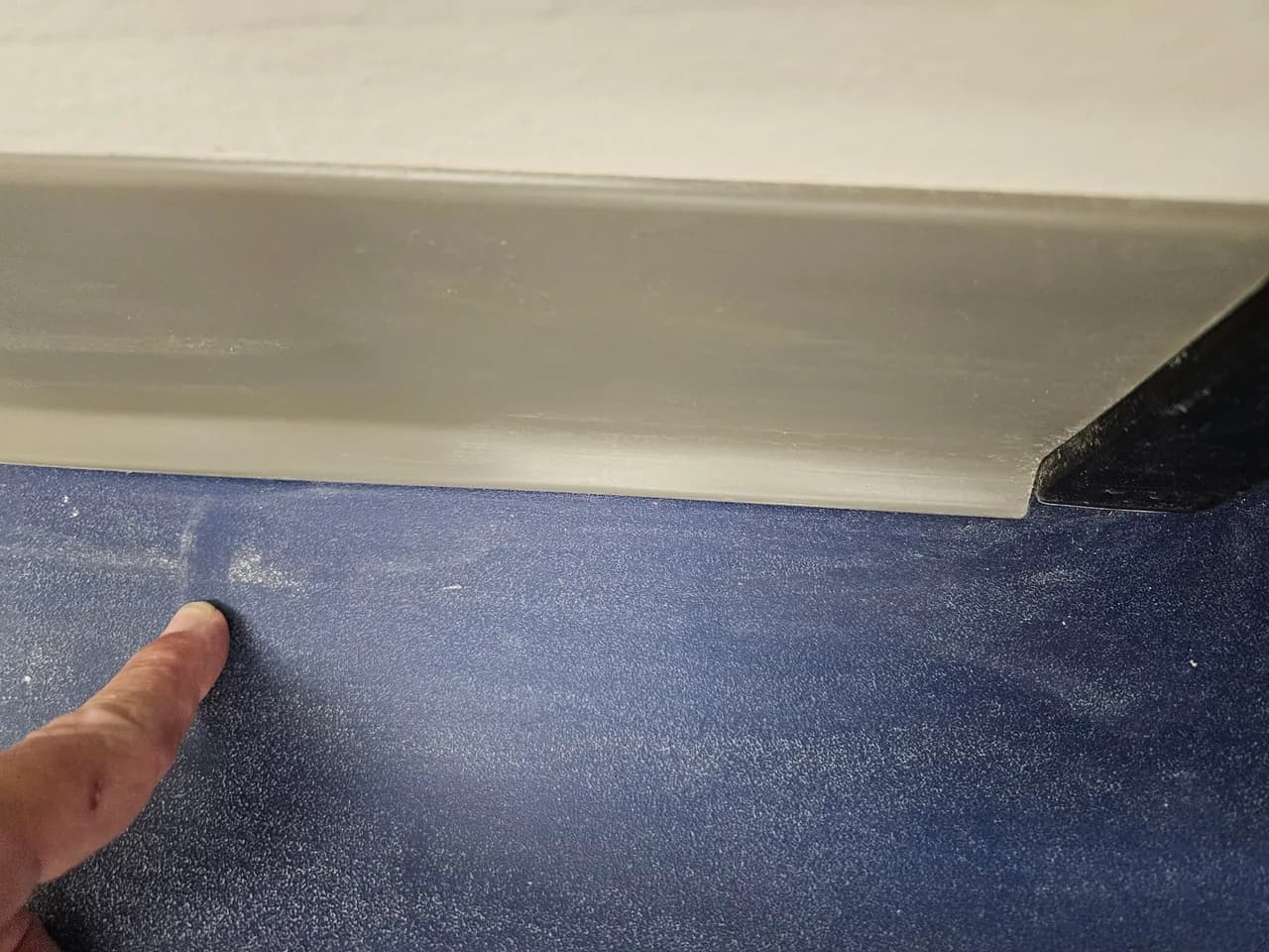 Finger indicating settled dust on a blue painted surface beside gray trim