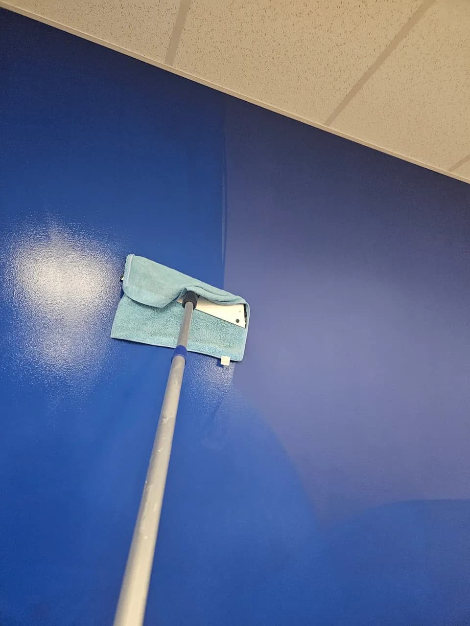 Microfiber pad on an extension handle cleaning a blue painted wall