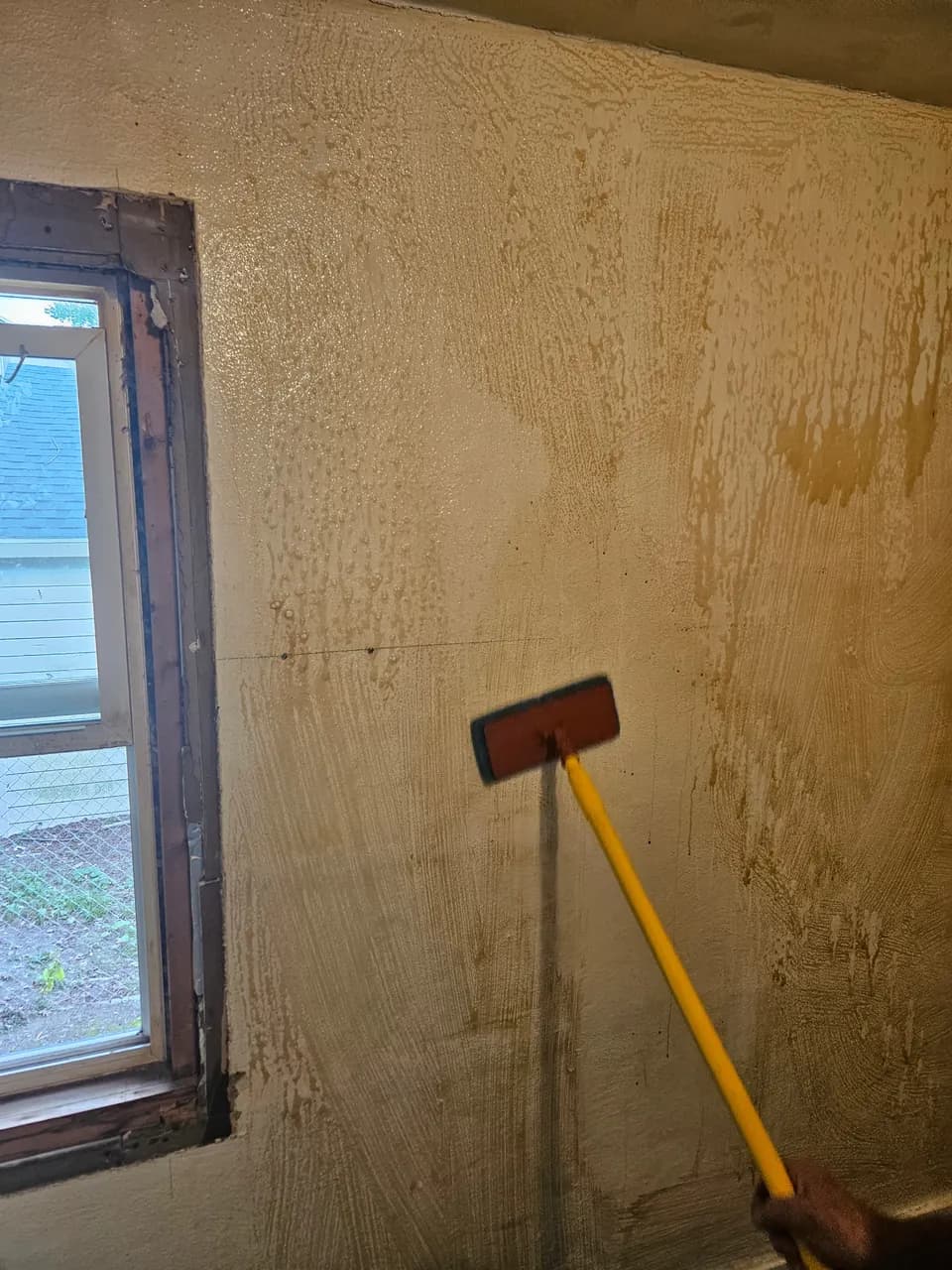 Cleaning pad on an extension handle against a wall with brown residue beside a window