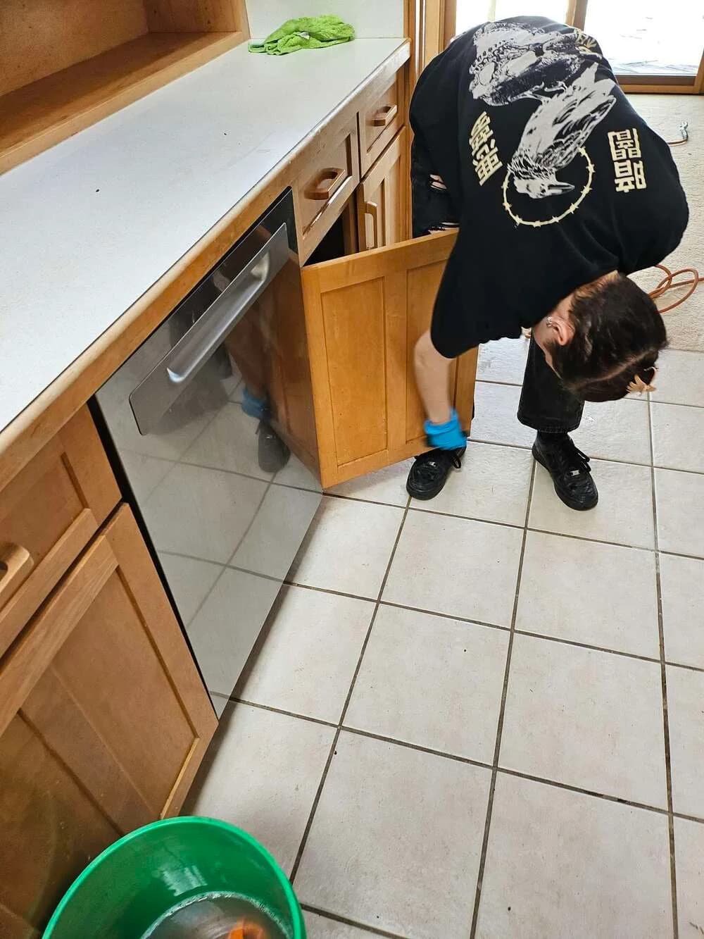 Technician scrubbing cabinet toe-kicks along a tile kitchen floor